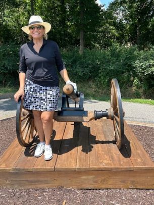 Woman sitting on a bench shaped like a cannon wheel, outdoors in a sunny park.